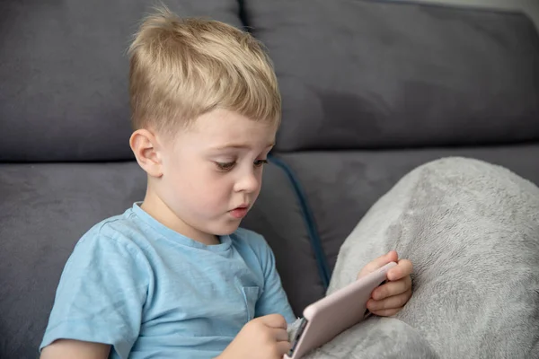 Lindo Niño Rubia Mira Teléfono Inteligente Sentado Sofá Casa Concepto —  Fotos de Stock