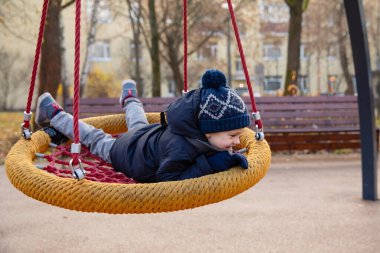 Mutlu, gülümseyen bir çocuk çocuk çocuk parkında salıncak sürüyor. Tatmin oldu. Salıncak sepeti, hamak. Çocukluk kavramı.