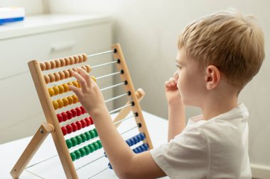 Şirin küçük sarışın oğlan masada siyahi çocuklarla ahşap banknotlarla meşgul. Odaklanmış, dikkatlice bakıyor. Montessori oyunları. Eğitim kavramı.