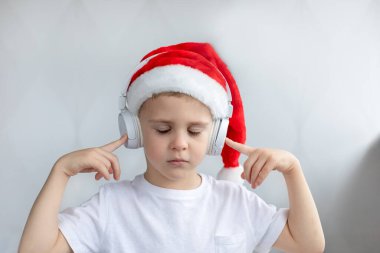 Noel şapkası takmış, kulaklık takmış, müzik dinleyen sevimli, küçük bir çocuk, o mutlu. Hafif arkaplan. Kış tatili kavramı.