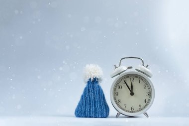 Bir dizi Noel aksesuarı, bir saat ve hafif kar arka planında mavi örülmüş bir şapka. Tasarım ve metin için alan. Kış tatili Yeni Yıl, Noel kavramı.