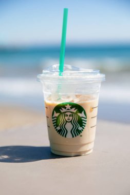 Antalya, Türkiye - 07.07.2021: Plaj ve mavi denizin arka planında buzlu soğuk kahve ile bir bardak Starbucks. Tatiller, deniz dinlenme konsepti.