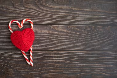 Çizgili karamelli lolipoplardan iki kalp ve koyu arkaplanda kırmızı yün iplikler. Tasarım ve metin için alan. Tatil kavramı, aşkım..