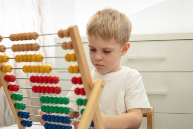 Şirin küçük sarışın oğlan masada siyahi çocuklarla ahşap banknotlarla meşgul. Odaklanmış, dikkatlice bakıyor. Montessori oyunları. Eğitim kavramı.