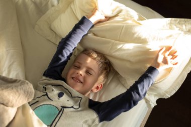 Pijamalı küçük bir çocuk uyanıyor, güneşin altında yatakta uzanıyor. Çocukluk kavramı, sağlık