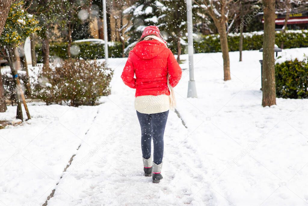 Young woman in red coat walking in the city on a snowy winter day