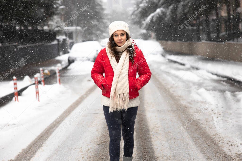 Young woman in red coat walking in the city on a snowy winter day