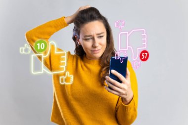 Young sad woman feeling unhappy and desperate holding mobile phone looking more dislikes than likes on her internet social media post in influencer obsession clipart