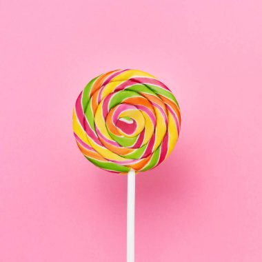 Pembe arka planda beyaz bir çubuk üzerinde gökkuşağı lolipop kıvrımı. Üst görünüm, alanı kopyala