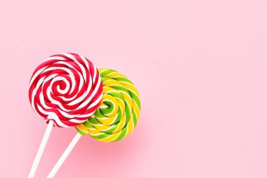 Açık pembe arka planda beyaz bir çubukta iki renkli lolipop. Üst görünüm, alanı kopyala
