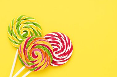 Parlak sarı bir arka planda beyaz bir çubukta üç renkli lolipop. Üst görünüm, alanı kopyala