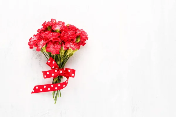 Cravos vermelhos flores buquê decorado com fita vermelha em um fundo de madeira branca — Fotografia de Stock