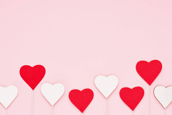 Valentines background. Red and white wooden hearts on a pink backdrop. Top view, copy space for text