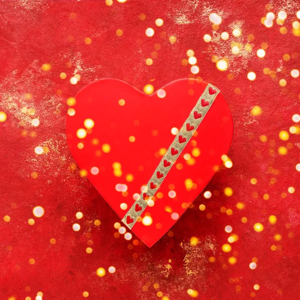 Caixa de presente vermelho em forma de coração decorado com fita dourada em um fundo vermelho brilhante. Vista superior — Fotografia de Stock
