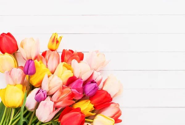 Buquê de tulipas coloridas brilhantes em um fundo de madeira branco. Cartão de felicitações. Espaço de cópia, flat lay — Fotografia de Stock