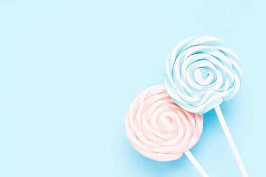 Açık mavi arkaplanda beyaz bir çubukta pembe ve mavi lolipoplar. Üst görünüm, alanı kopyala