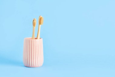 Mavi arka planda seramik bir tutacakta iki bambu diş fırçası. Çevre dostu, sıfır atık kavramı