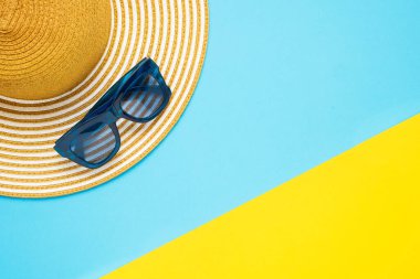 Yaz tatili kavramı. Plaj aksesuarları, çizgili şapka ve sarı-mavi arka planda güneş gözlüğü.