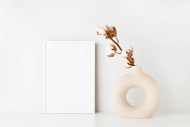 Beyaz çerçeve maketi ve seramik vazo. Beyaz bir masanın üzerinde beyaz bir dal var. Işık duvarının yanında. Metin için alanı kopyala