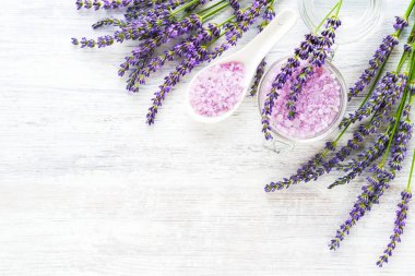Lavender aroma bath salt and lavender flowers on white wooden background. Spa, skincare concept. Top view, copy space. Selective focus
