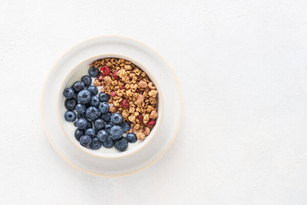 Bowl of homemade yogurt with granola and blueberries on a light background. Top view, copy space for text