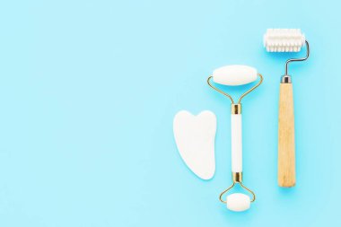 İki farklı masaj silindiri ve açık mavi arka planda yüz için gua sha masaj aleti. Bencillik, cilt bakımı. Boşluğu kopyala