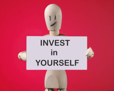 Kırmızı arka plandaki ahşap bir adamın elindeki bir kağıt karta kendin yatırım yap..