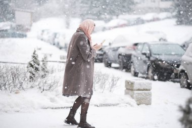 Kar yağan arka planda bir kadın telefonuna bakar.