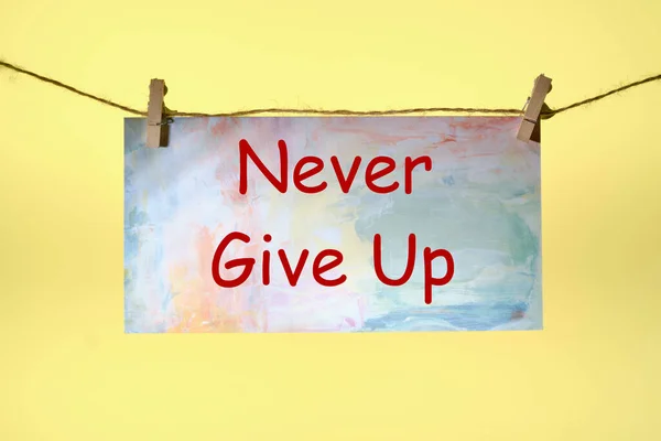 Never give up text written on paper suspended from a rope on a yellow background ,business idea — Stock Photo, Image