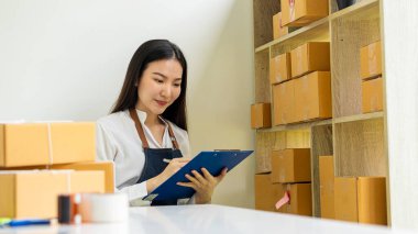 Güzel Asyalı KOBİ işletme sahibi online alışverişte dizüstü bilgisayarda çalışıyor ve evdeki masada paket kutuları var - KME çevrimiçi iş fikri ve kutu teslimatı.