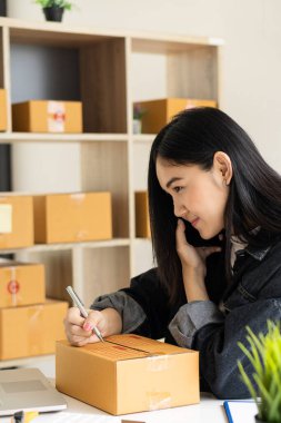 Güzel Asyalı KOBİ işletme sahibi online alışverişte dizüstü bilgisayarda çalışıyor ve evdeki masada paket kutuları var - KME çevrimiçi iş fikri ve kutu teslimatı.