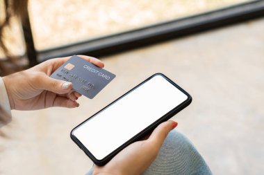 Elinde boş ekran ve kredi kartı bilgileriyle akıllı telefon tutan genç bir kadın internet üzerinden sipariş vermek ve internet bankacılığı üzerinden ödeme yapmak için kredi kartı bilgilerinizi uygulama veya web sitesine girin.
