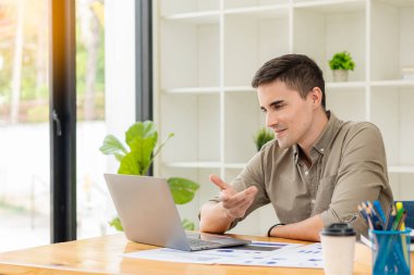 Genç işadamı, ofiste dizüstü bilgisayar ve hesap makinesiyle finansal rapor verilerini analiz ediyor ve beyin fırtınası yapıyor. Mali muhasebe ve yatırımla çalışma kavramı