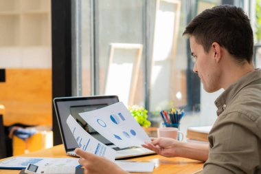 Genç işadamı, ofiste dizüstü bilgisayar ve hesap makinesiyle finansal rapor verilerini analiz ediyor ve beyin fırtınası yapıyor. Mali muhasebe ve yatırımla çalışma kavramı