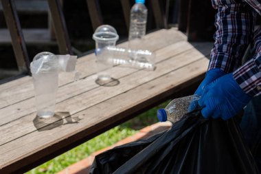 Plastik şişelerin yakın çekim elleri. Gönüllüler, arka plandaki çöp torbalarında plastik şişe biriktiriyorlar. Ekoloji konsepti, çöpleri toplayan genç bir adam parktan geri dönüşümlü plastik şişeler topluyor..