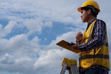 Elinde kağıt Pam ve kalem tutan genç bir mühendis gökyüzünden bir binayı inceliyor..