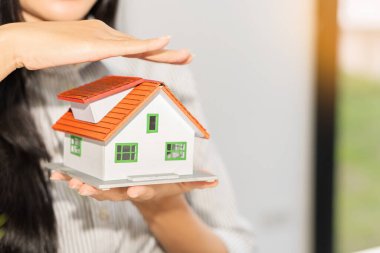 Elinde küçük ev modeli, ev ve sigorta koruması ve kontrol kavramı tutan genç bir kadın..