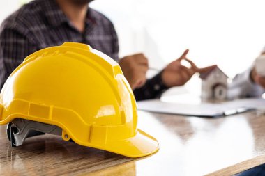 Önde sarı mühendis miğferi müşterilerle ev kredisi anlaşması yapan ve ev sigortası sözleşmesi imzalayan satış temsilcisi.