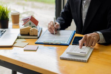 İş adamı ya da satış temsilcisi kontrat belgeleri ve hesap makinesiyle ofiste çalışıyor. Faiz ve vergileri hesaplamak ve müşterilere satın alma ve kiralama konusunda tavsiyede bulunmak