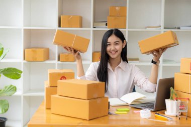 Küçük bir işletmenin portresi, KME Sahibi, Asyalı Kadın Girişimci Fatura kutuları üzerinde çalışır ve kutuları hazırlamak için çevrimiçi siparişleri işaretler. Müşterilere satıyorum. Çevrimiçi KOBİ iş fikri.