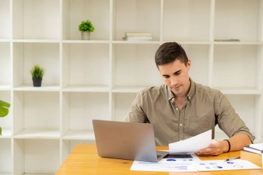 Elinde kalem tutan işadamı, pazarlama planını hesap makinesi ve dizüstü bilgisayarla ofis finans ve muhasebe kavramlarındaki ahşap masa üzerinde analiz etmek için grafiğe işaret ediyor.