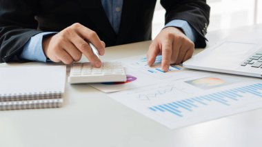 Bir iş adamı elinde bir kalem tutarak hesap makinesine basar ve masasında bir dizüstü bilgisayarla şirketin aylık mali raporlarını ya da ofis kârlarını hesaplar ve analiz eder. finansal iş muhasebe kavramı