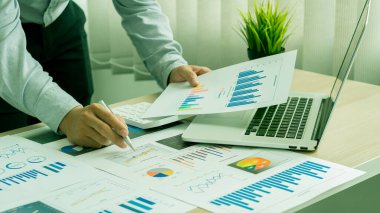 Bir iş adamı elinde bir kalem tutarak hesap makinesine basar ve masasında bir dizüstü bilgisayarla şirketin aylık mali raporlarını ya da ofis kârlarını hesaplar ve analiz eder. finansal iş muhasebe kavramı