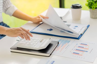 Bir iş adamı elinde bir kalem tutarak hesap makinesine basar ve masasında bir dizüstü bilgisayarla şirketin aylık mali raporlarını ya da ofis kârlarını hesaplar ve analiz eder. finansal iş muhasebe kavramı
