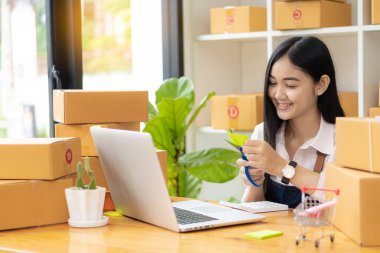 Genç Asyalı bir kadın, girişimci, evde bilgisayarla çalışan bir iş sahibi. Çevrimiçi alışveriş hizmeti, KME küçük işletme girişimcisi veya kutularla çalışan bağımsız Asyalı kadın.