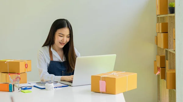 Young Asian woman, entrepreneur, a business owner who works with computers at home. Online shopping delivery, SME small business entrepreneur or independent Asian woman working with boxes.