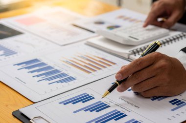 Kalemi olan bir işadamı finans tablosuna işaret eder ve mali tablo verilerini ve iş dünyasının yatırım ve pazar durumunu değerlendirmeye yönelik pazar planını açıklamak için analiz eder..