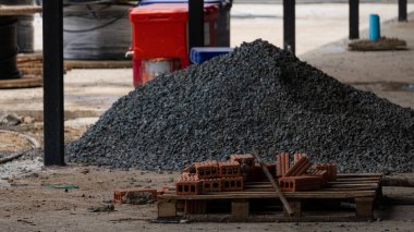 Kırmızı tuğlalar ve kum yığınları, inşaat alanında güçlendirilmiş beton yığınları yapmak için zeminde inşaat malzemeleri..