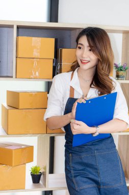 Asyalı bir kadın girişimcinin sahibi olan küçük işletme kuruluşu KME, ürünlere kutu hazırlamak için çevrimiçi siparişleri kontrol etmek üzere posta kutuları ve dizüstü bilgisayarlarla çalışıyor. Fikirleri internette sat