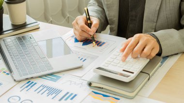 Harcamaları hesaplamak için parmaklarını hesap makinesine bastıran bir işadamı vergi bilgilerini hesaplamaktır. ve büyüme ve ilerleme ile iyi durumda olan finansal hisse senedi grafiklerini analiz etmek..